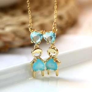 Collier doré avec deux personnages ornés de zircons bleu clair en forme de cœur sur blanc