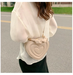 Fashion heart-shaped beige crossbody bag with quilted texture shown on a female model