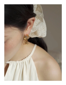 Close-up of golden irregular wavy hoop earring worn by a model in an elegant setting
