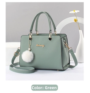 Green leather handbag detail with gold hardware and a fluffy pom-pom charm decoration