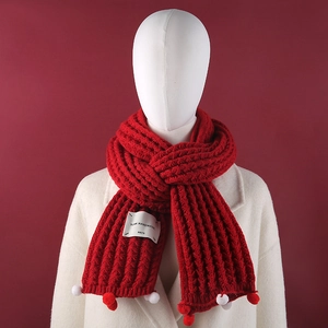 Close-up of red knit scarf featuring white pom-poms and handmade fabric label detail