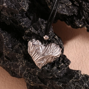 Detailed macro shot of silver heart pendant with textured lava surface on black cord