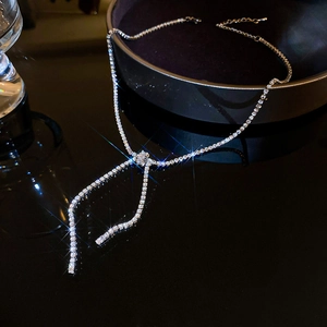 Macro detail of silver-tone bow necklace with sparkling crystals and knot tassel design