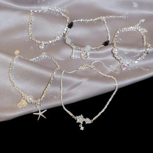 Dettaglio di cinque bracciali argentati con perle e ciondoli a stella su seta grigia
