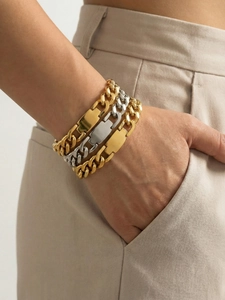Detail of layered chunky link gold and silver bracelets with polished metal plates
