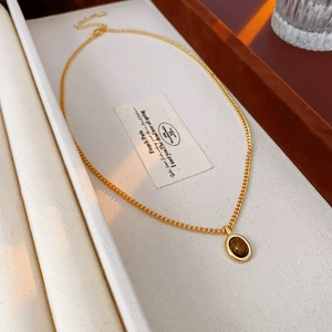 Détail d'un collier doré vintage avec pendentif ovale en pierre œil de tigre sur tissu