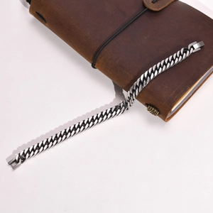 Detail shot of a silver Cuban link bracelet placed on a vintage leather notebook cover
