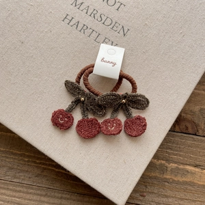 Detailed close-up of cute knitted cherry hair ties with smiling face embroidery
