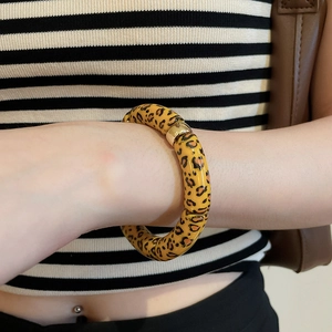 Detail of chunky leopard print resin bangle with gold metal clasp on a female wrist