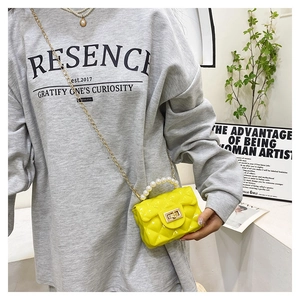 Detail of yellow quilted mini bag featuring pearl handle and gold chain on model