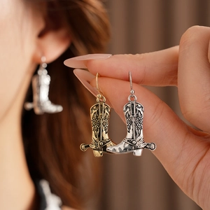 Détail des boucles d'oreilles bottes de cowboy vintage avec gravure florale or et argent