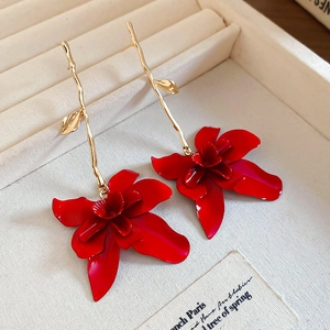 Macro shot of long red orchid flower earrings with golden branches on beige fabric
