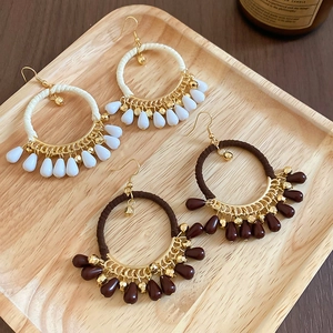 Close-up of bohemian woven rope hoop earrings with teardrop beads on a wooden tray