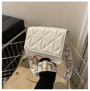 Detailed view of white quilted crossbody bag with a wide decorative patterned strap