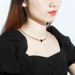 Gold flat snake bone chain necklace with a black round shell pendant on model neck