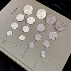 Detail of silver drop earrings with graduated textured round metal disks and long tassels