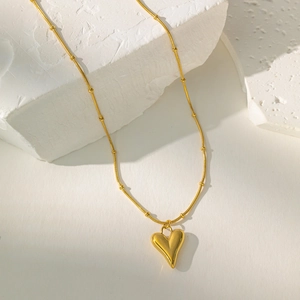 Detailed view of a gold heart pendant necklace with pearl on a white stone background