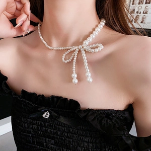 Dettaglio della collana di perle bianche con ciondolo a fiocco indossata da una modella