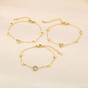 Gold stainless steel bracelet set featuring heart, butterfly, and flower pendants on fabric
