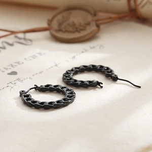 Macro shot of black chain-link hoop earrings on textured paper with vintage wax seal