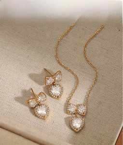 Close-up of golden bow and heart jewelry set with sparkling zircon on beige fabric