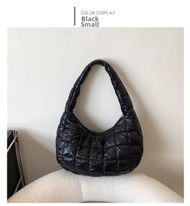 Detail view of small black quilted puffer bag on white textured stool surface