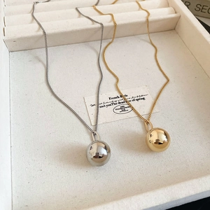 Detail view of gold and silver ball pendant necklaces on a cream velvet jewelry tray