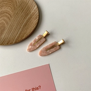 Macro detail of two pink marble-textured acetate hair clips with gold metal base