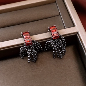 Macro shot of silver earrings featuring red square gems and long black beaded tassels