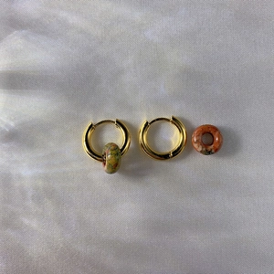 Detail of 18k gold earrings with natural stone pendants on soft satin fabric