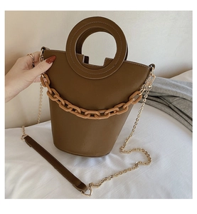 Detail of brown bucket bag featuring a round handle and thick decorative resin chain