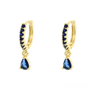 Dettaglio di orecchini a cerchio dorati con zirconi blu e pendente a forma di goccia