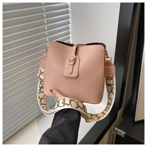 Close-up of pink lychee leather bucket bag with printed wide shoulder strap and gold buckle