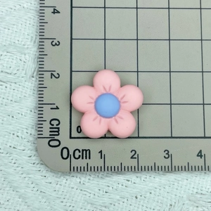 Top view of a 2.5cm pink frosted flower resin charm on a grid cutting mat for DIY crafts