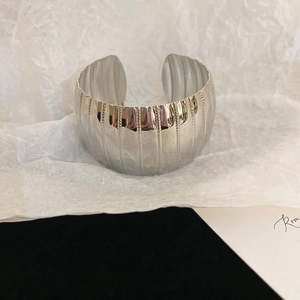 Close-up of wide silver metal cuff bracelet featuring a textured vertical stripe pattern