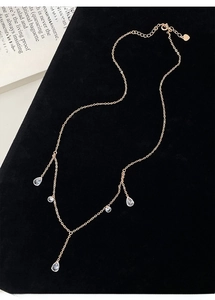 Close-up of gold Y-chain necklace with teardrop and round zircon charms on black velvet