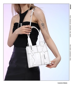 Detail der weißen Lackleder-Handtasche mit schwarzen Nähten und 'FASHION'-Gurt