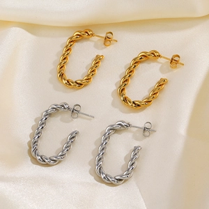 Boucles d'oreilles créoles torsadées dorées et argentées sur fond de satin de soie