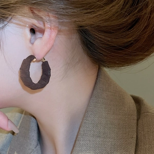 Close-up of deep brown textured fabric hoop earring worn by a model in warm lighting