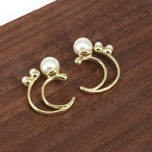 Detail of gold double C-shaped earrings with large pearls on dark wood surface