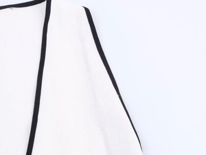 Close-up of white linen dress showing refined black piping and knitting texture