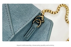 Close-up of light blue cross-grain leather bag with gold metal chain and buckle