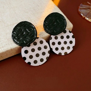 Polished black textured and white polka dot acrylic earrings on a beige linen display box