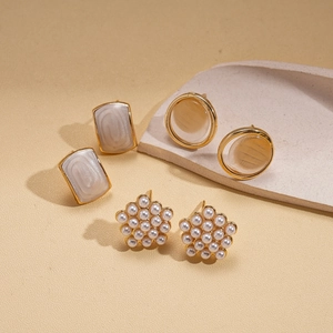 Détail de trois paires de boucles d'oreilles dorées avec perles, œil de chat et fleurs