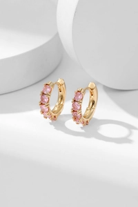 Close-up of gold hoop earrings with claw-set pink zircons on a white platform