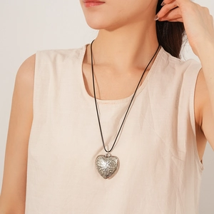 Detailed shot of engraved silver heart pendant with black wax cord on a model