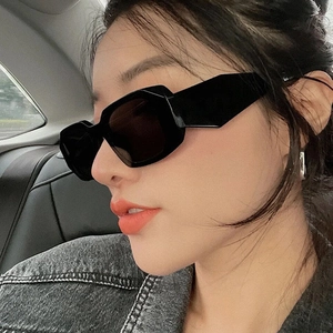 Close-up of black geometric square sunglasses worn by a model in a car setting