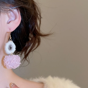 Primo piano di orecchini a pompon bianchi e rosa indossati da una modella in inverno