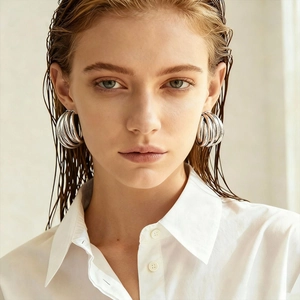 Close-up of model wearing large multi-layered geometric silver stud earrings
