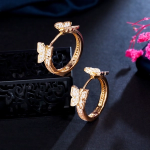 Close-up of gold butterfly hoop earrings with sparkling stones on a black jewelry box